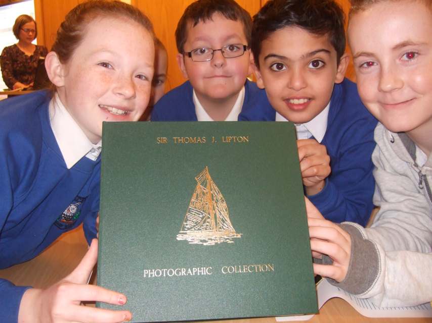 5 primary school aged children hold a green book titled "Sir Thomas J. Lipton - Photographic Collection"